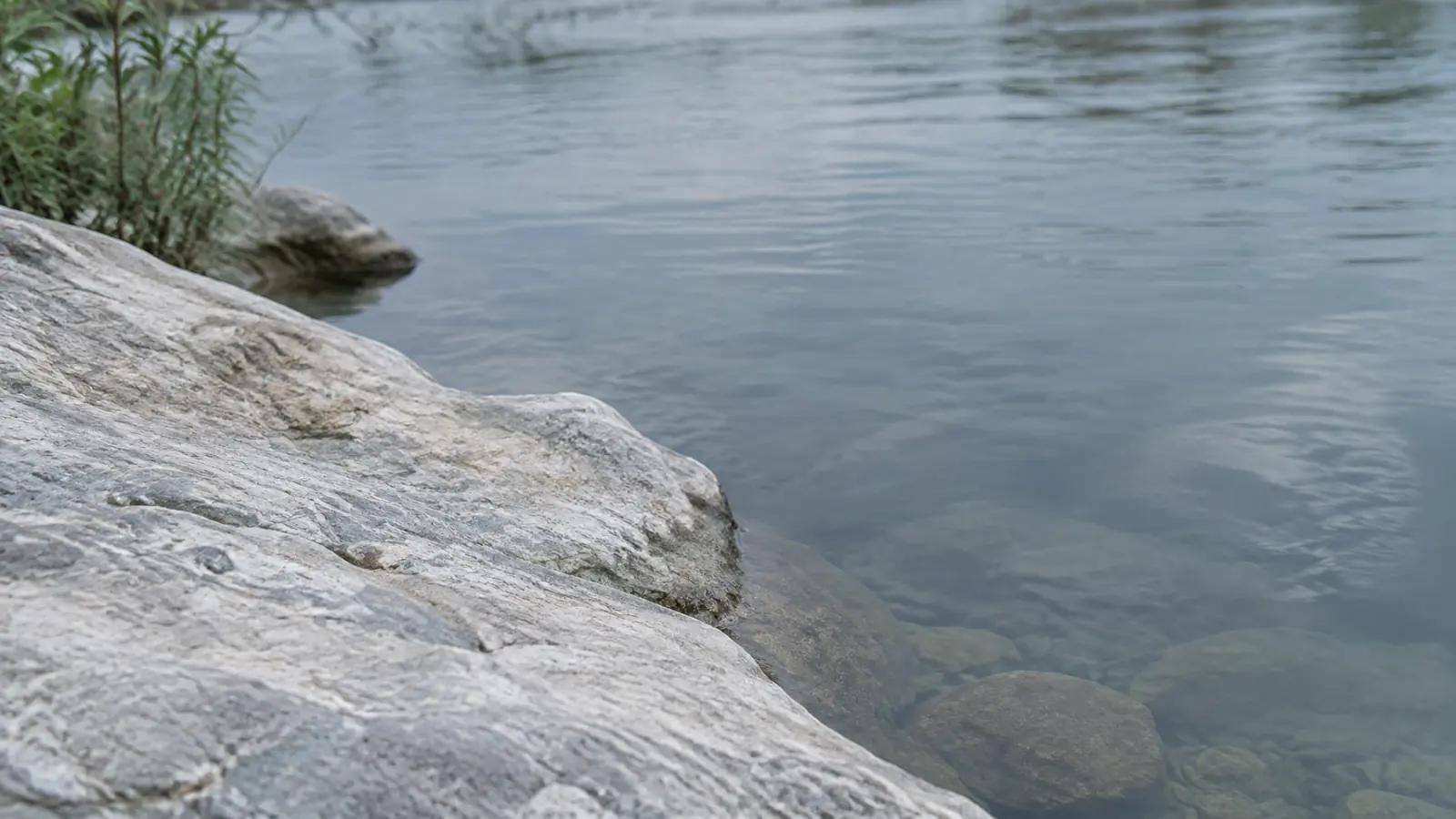 Pale stone meeting still blue-grey water at a quiet river edge