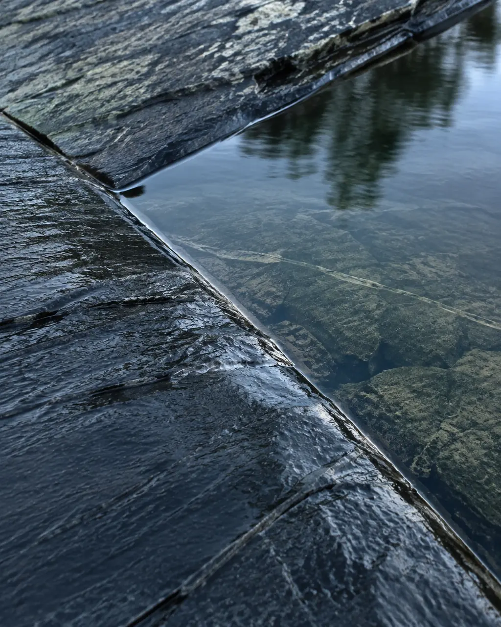 Intersecting wet slate stone planes beside a thin line of still water