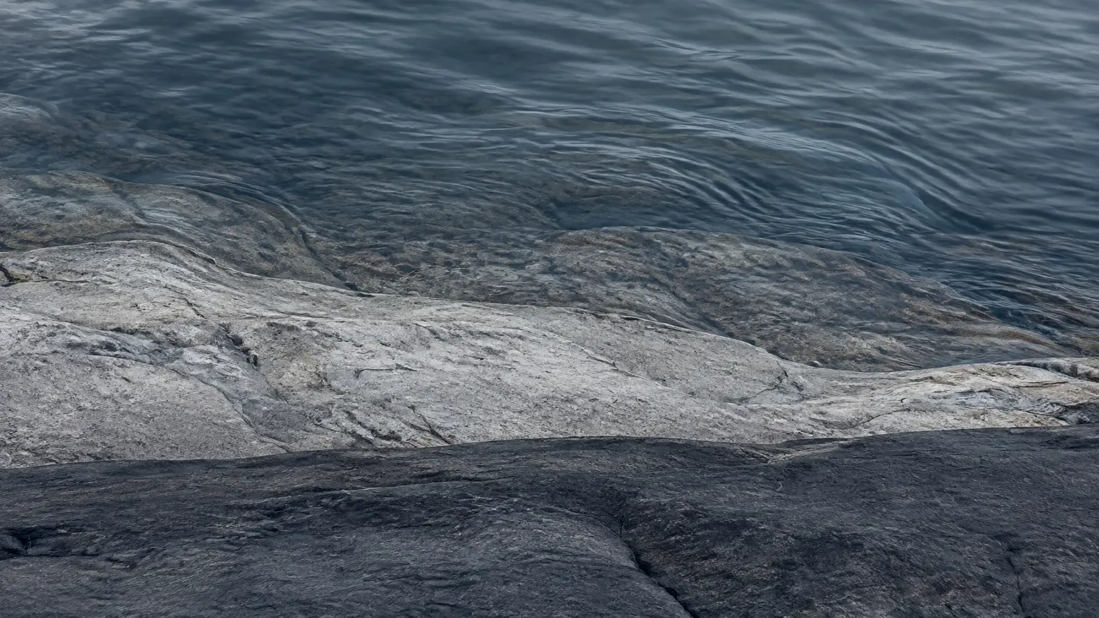 Still blue-grey water meeting pale stone and dark slate at a quiet river edge